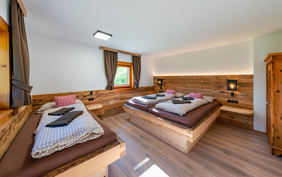 Tiroler Schlafzimmer mit Doppelbett und Einzelbett, eingerichtet mit Altholz, Sonnenlampen und Eichenfußboden.